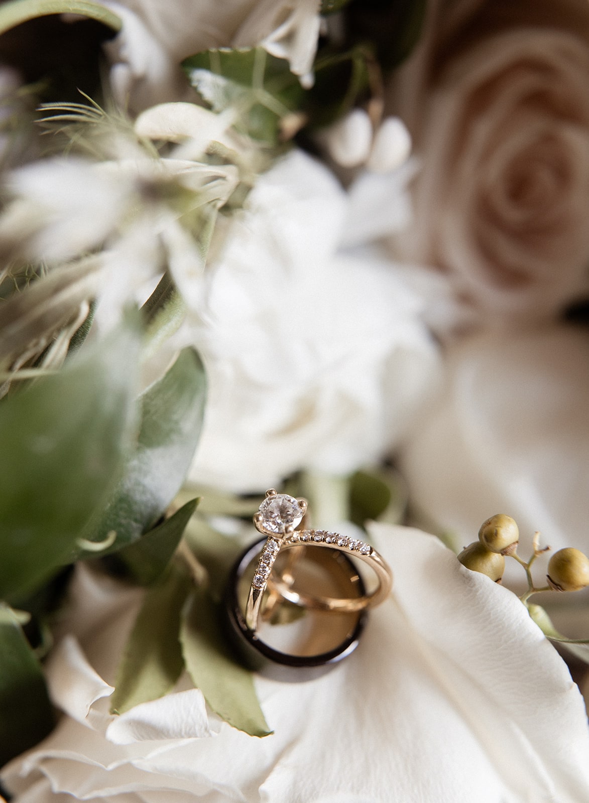 Diamond and gold and black wedding bands rest on top of white wedding flowers