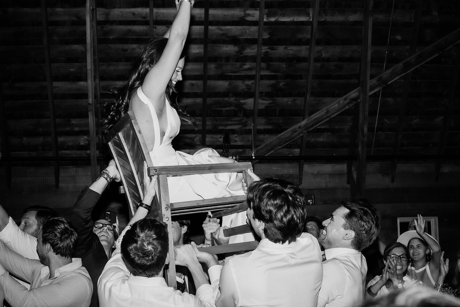 Bride gets carried on a wood chair during the dance reception at Firelight Farm