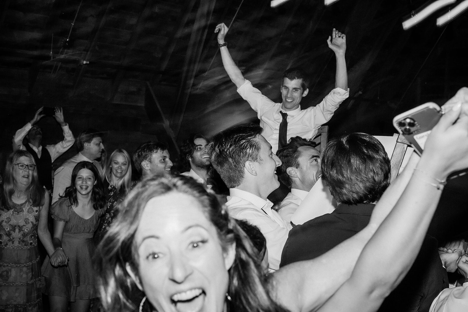 Bride gets carried on a wood chair during the dance reception at Firelight Farm