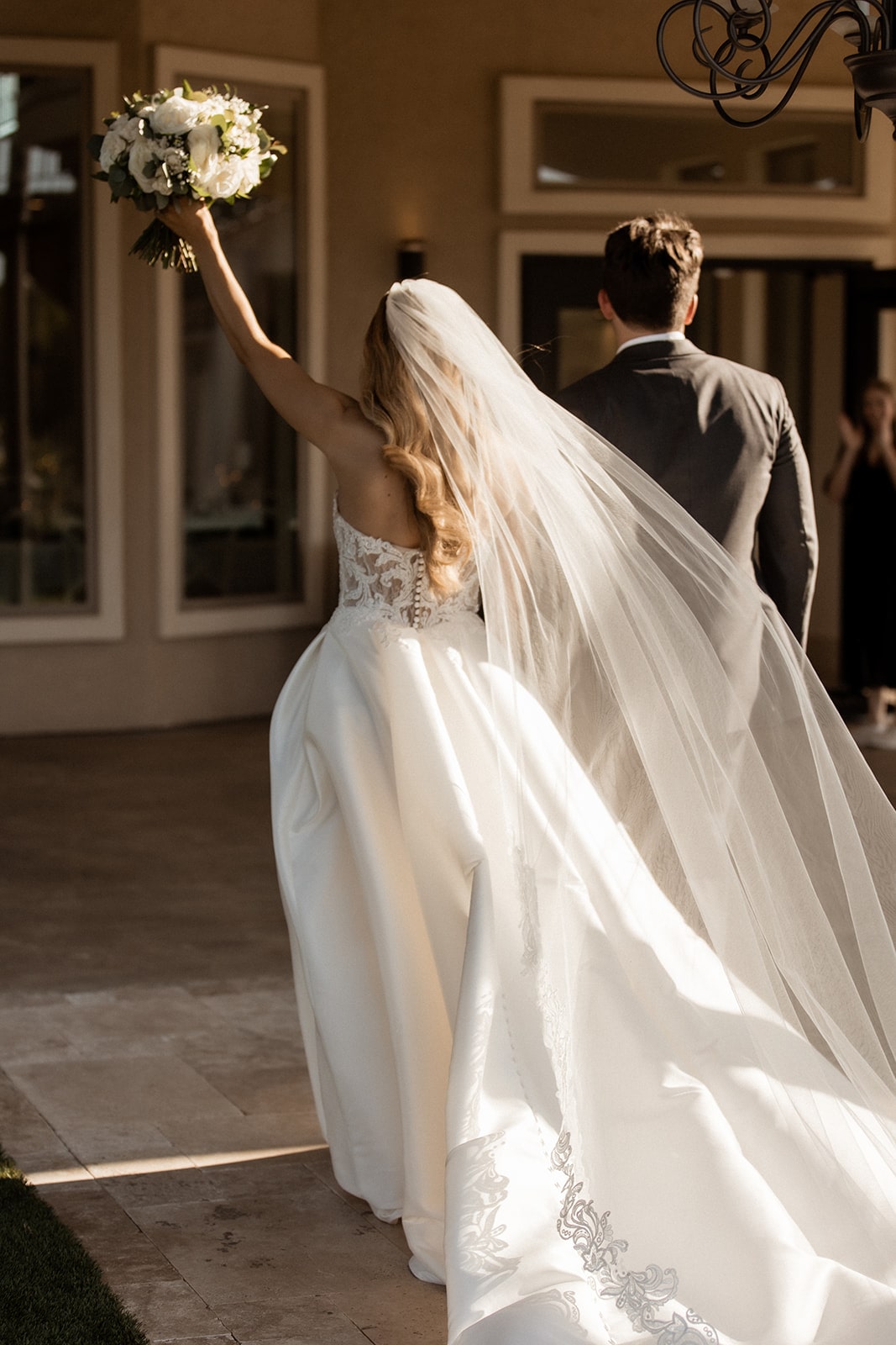 Bride lifts her bouquet into the air as she and groom exit their wedding aisle