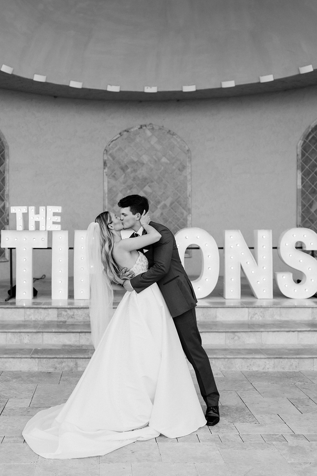 Groom dips bride for a kiss in front of custom marquee letter sign at their north Texas wedding