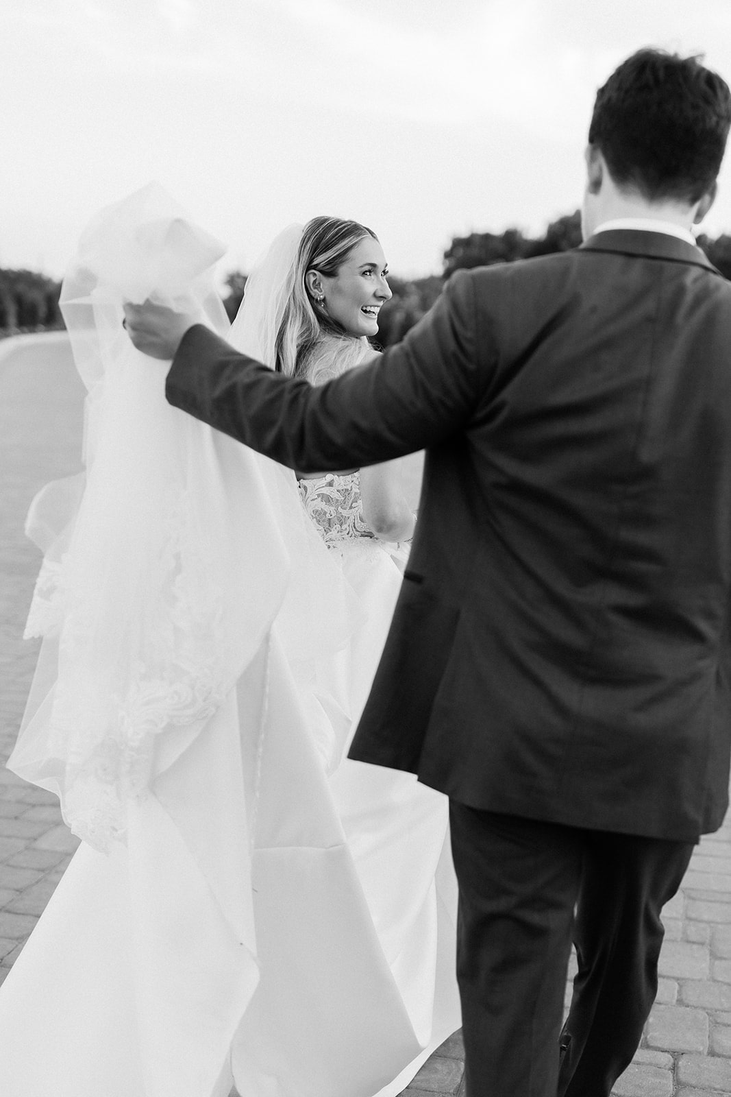 Groom lifts bride's wedding dress train as they walk across the grounds at D'vine Grace Vineyard