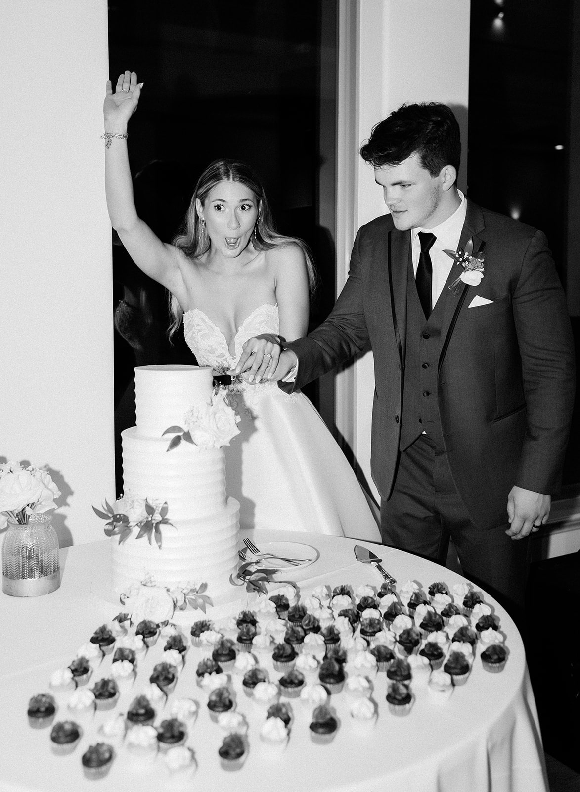 Bride makes a funny face as she and groom cut their three tier white wedding cake at their wedding reception in Fort Worth, Texas