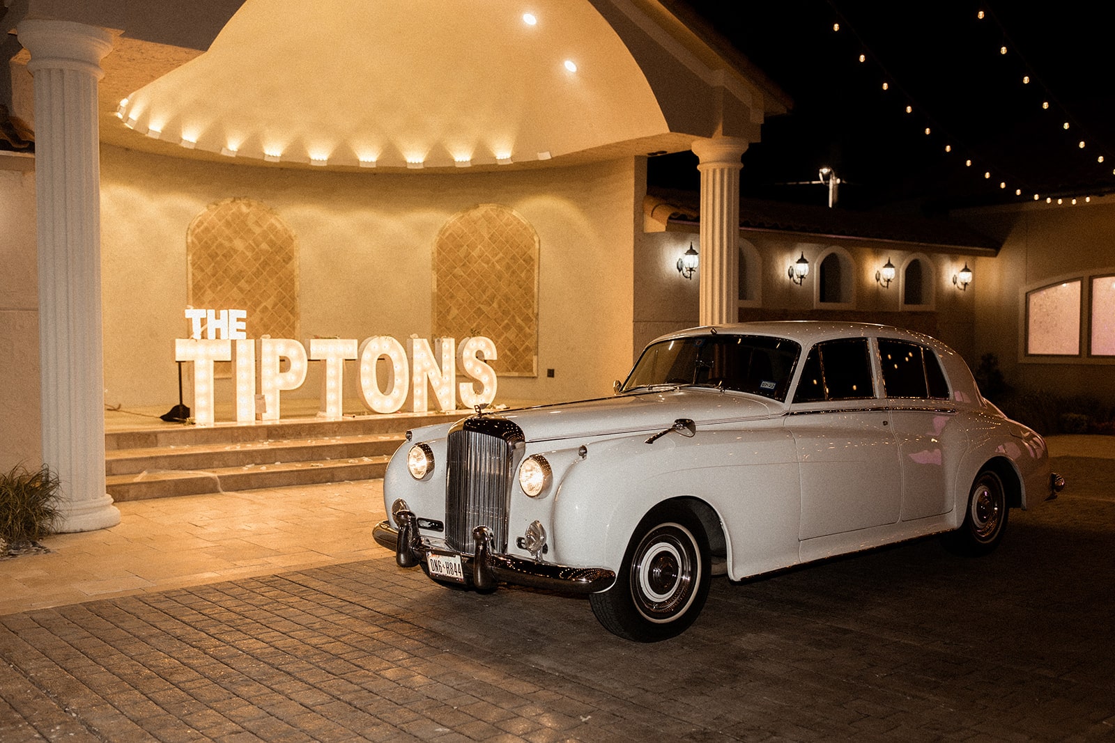 White vintage car sitting in front of a custom marquee lit sign