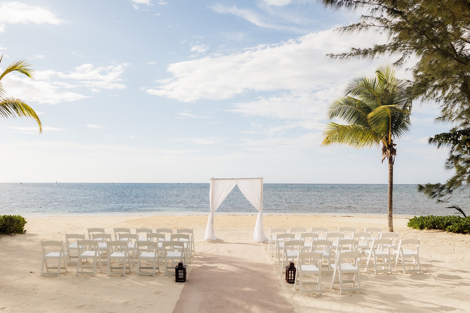 White wedding canopy with white wood chairs lined up on a sandy beach in Jamaica