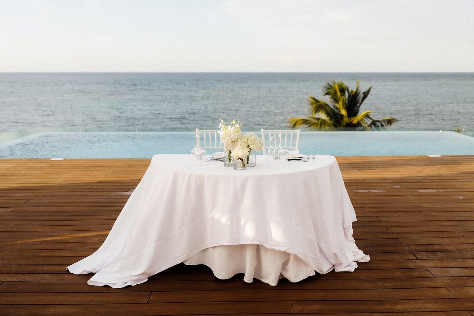 White sweetheart table sitting on a wood deck in front of the ocean at Excellence Oyster Bay resort in Jamaica