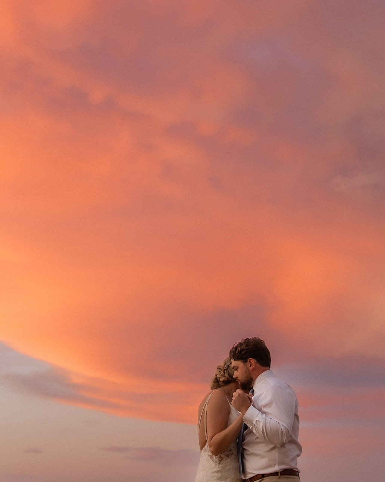 Orange and pink sunset colors light the sky while bride and groom share a first dance at their Jamaica wedding in Montego Bay