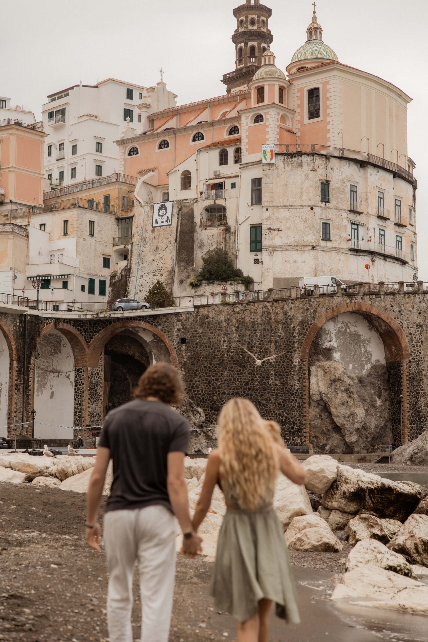 Couple holds hands and walks across the beach during their Italy post-wedding session