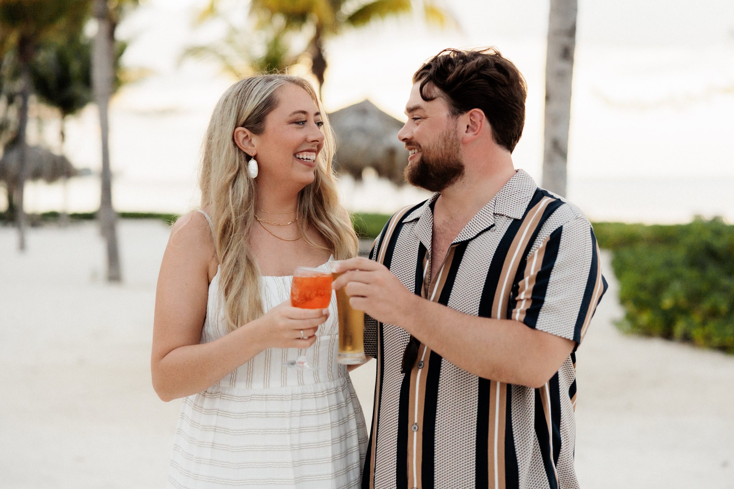 Bride and groom hold cocktails on the beach during their destination wedding welcome reception