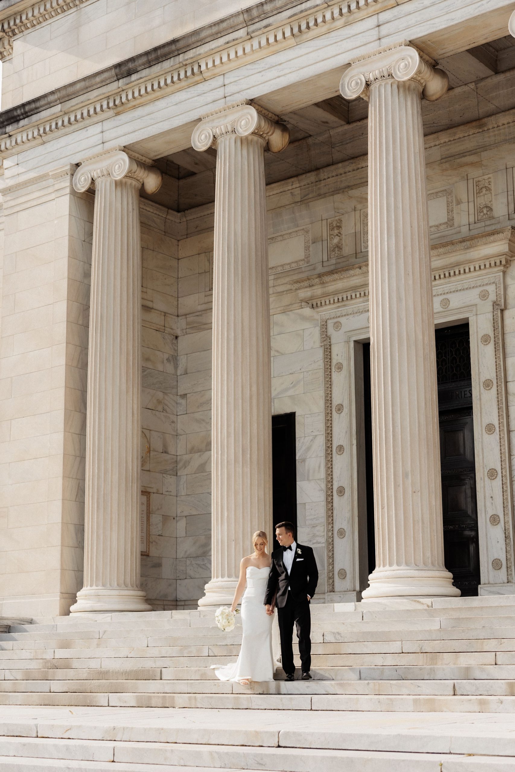 Bride and groom hold hands as they walk down the steps for their photos at the Cleveland Museum of Art