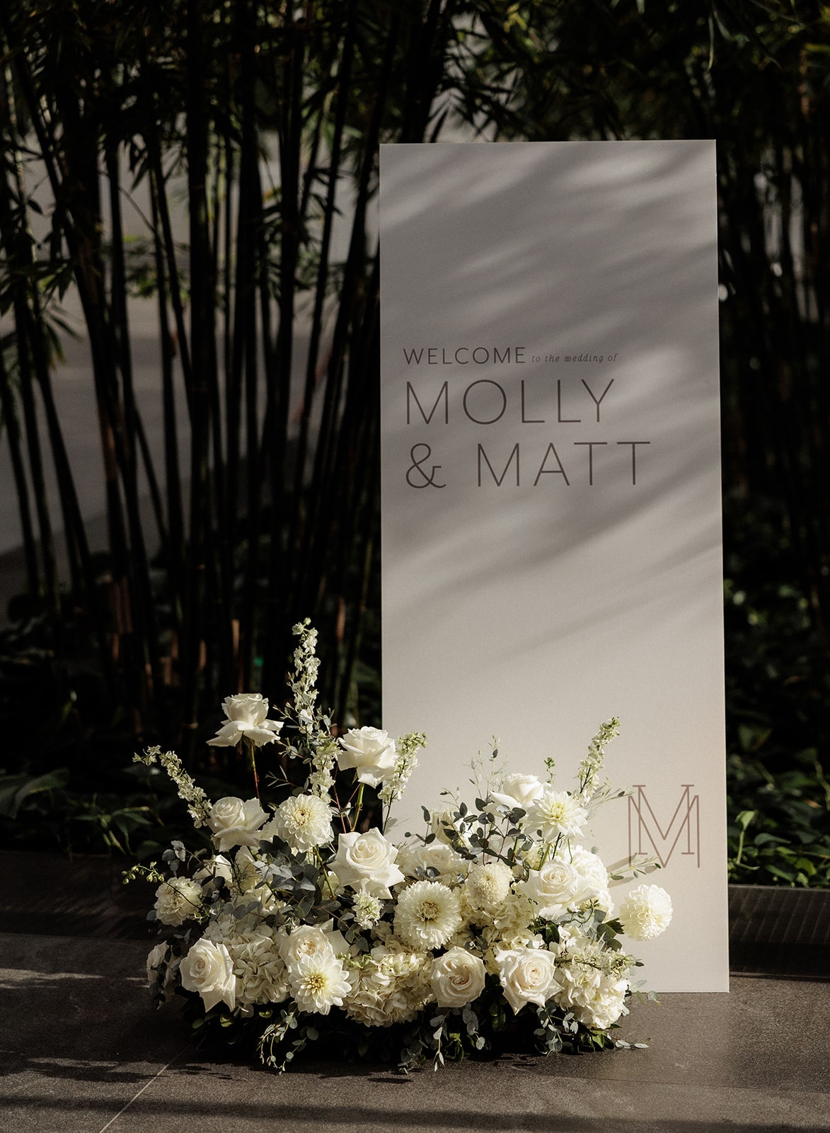 White modern wedding welcome sign with white flower arrangement at the base