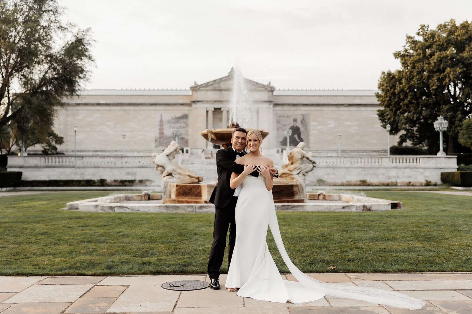 Groom hugs bride from behind during their wedding photos in front of an art gallery in Ohio